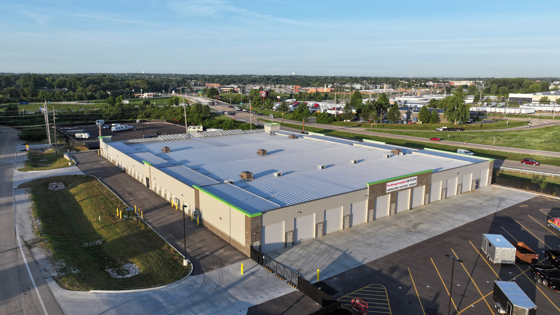 Aerial view of a large white-roofed industrial warehouse with loading bays, surrounded by roads, parking lots, and green landscape.