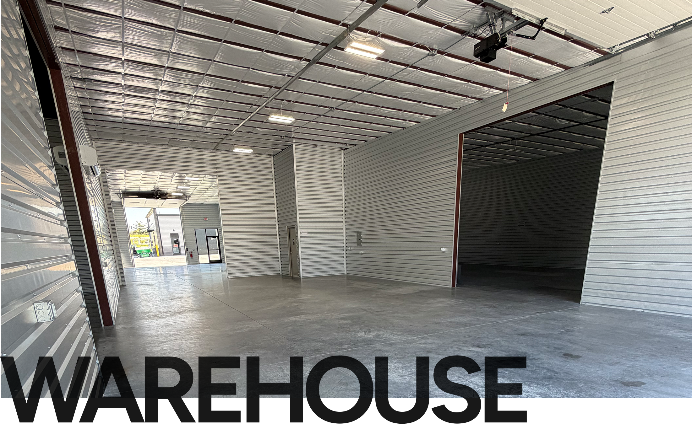 Interior of an industrial warehouse with metal panel walls, concrete floor, and multiple bay doors along the sides.